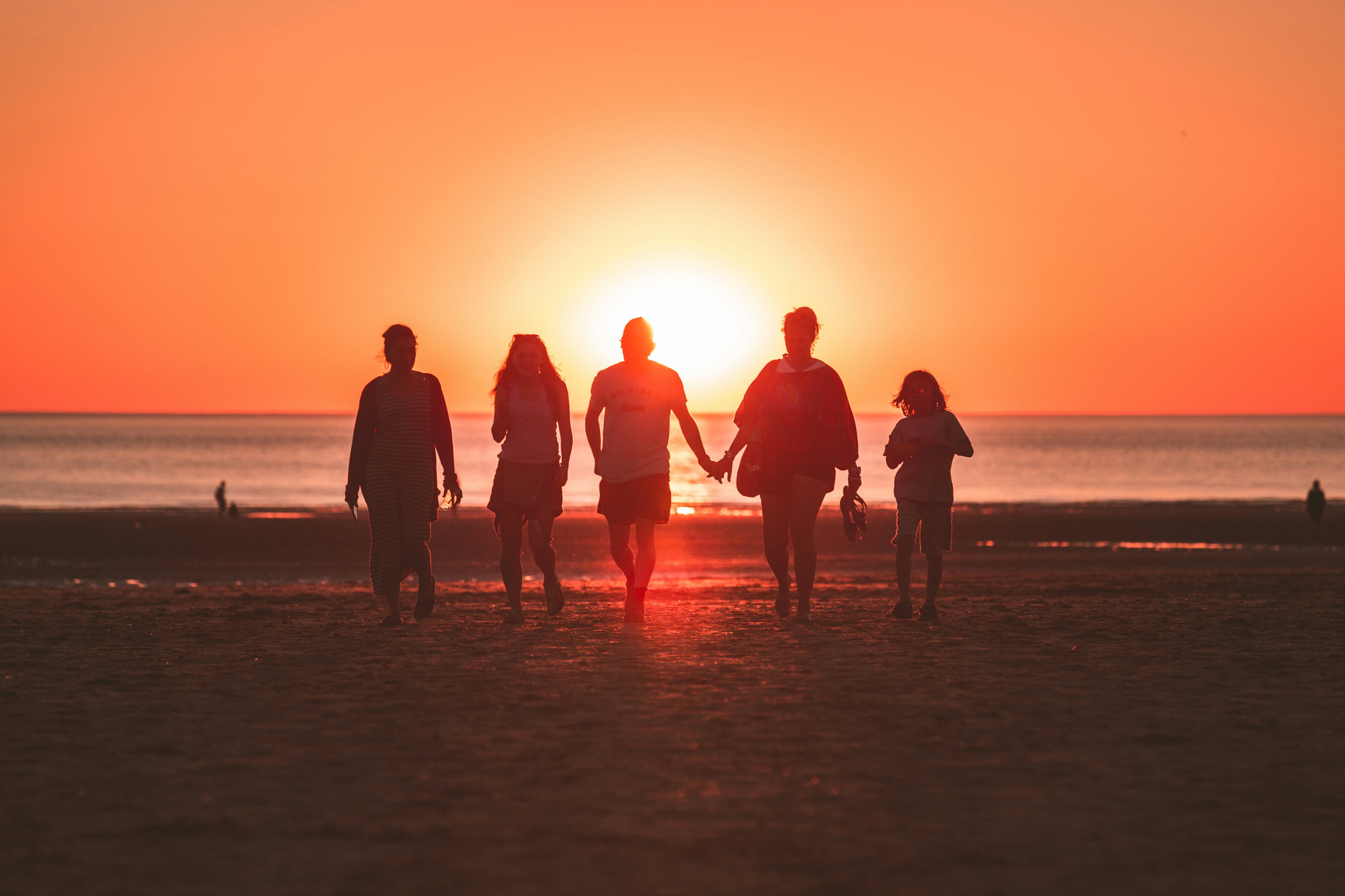 Five friends walking together on a beach at sunset